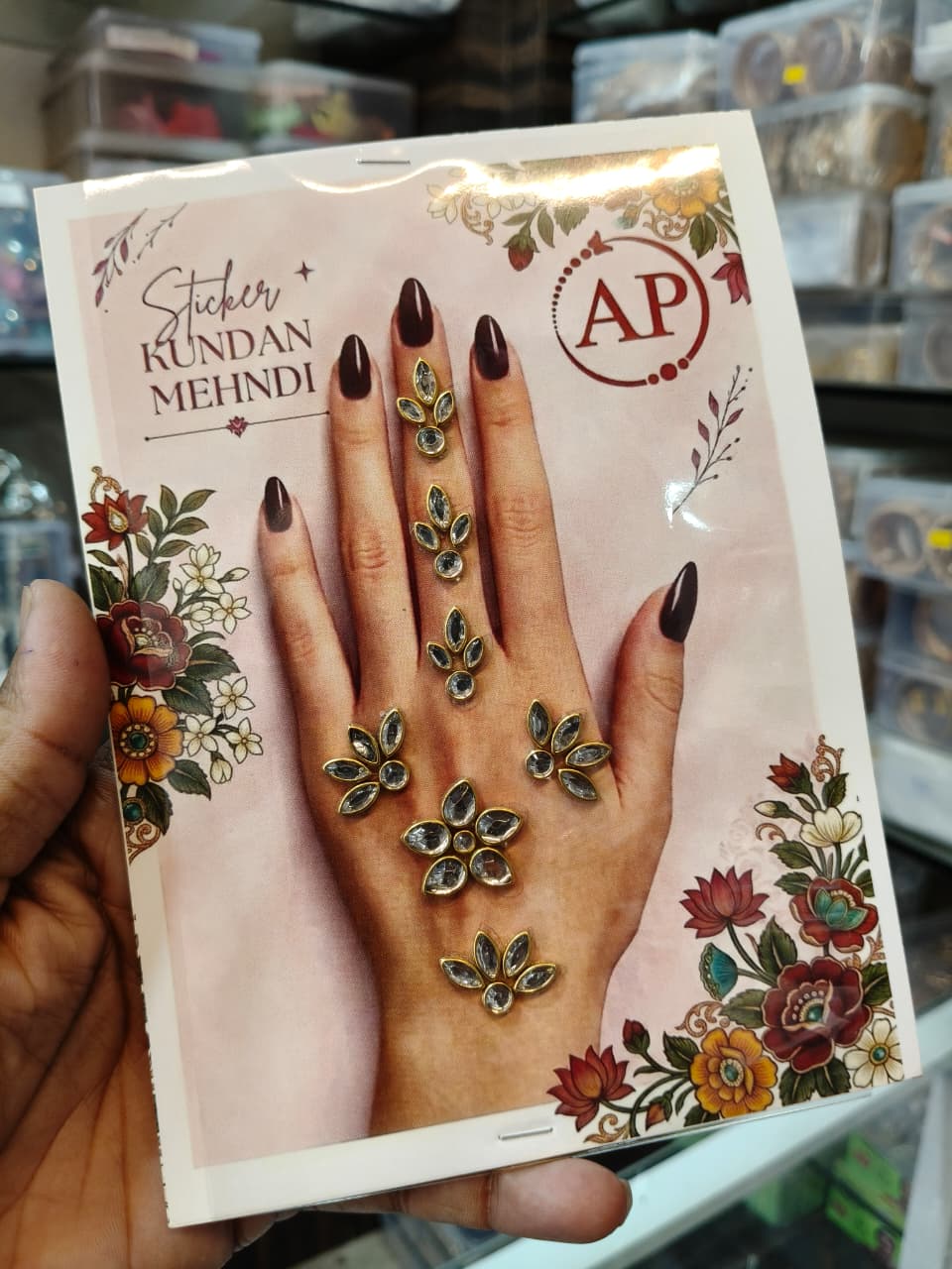 Kundan mehndi sticker sheet showing gold-tone teardrop stones and floral decorative pieces on a pink card